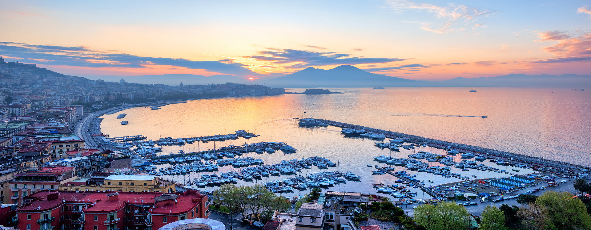 Harbor scene with boats and buildings at sunset, Vesuvius in the background
