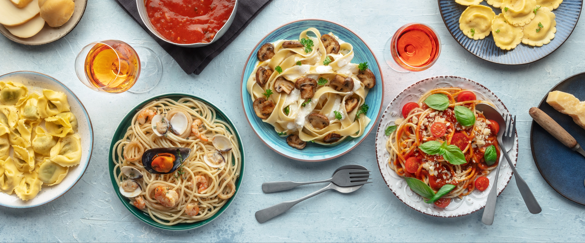Assorted pasta dishes on a light blue tablecloth with side dishes.